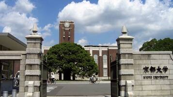 A university entrance with a large tree, a clock tower, and stone pillars with inscriptions.