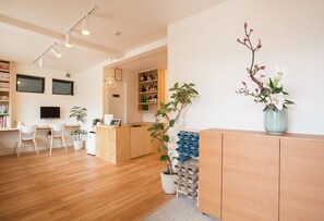A reception area with a wooden desk, chairs, a TV, and a plant. - Mulan Hostel (Kyoto)