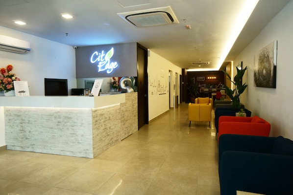 A hotel reception area with a marble counter, a neon sign, and a seating area with colorful sofas.