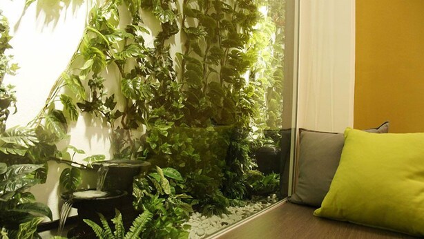 A room with a small indoor garden, a water feature, and a wooden bench with a green cushion. - City Edge Hotel (Kuala Lumpur)