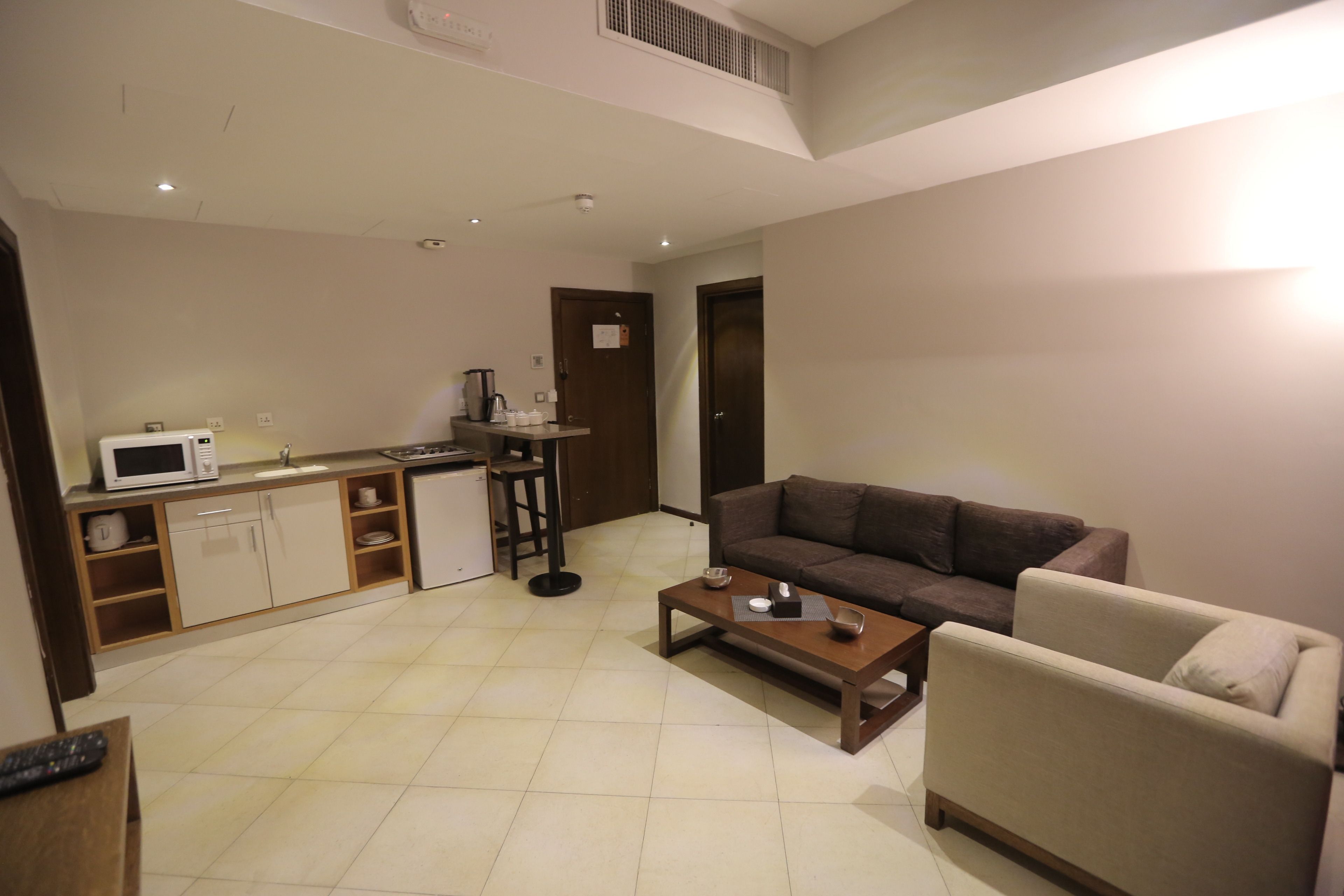A living room with a sofa, a coffee table, and a kitchen area with a microwave and a kettle.