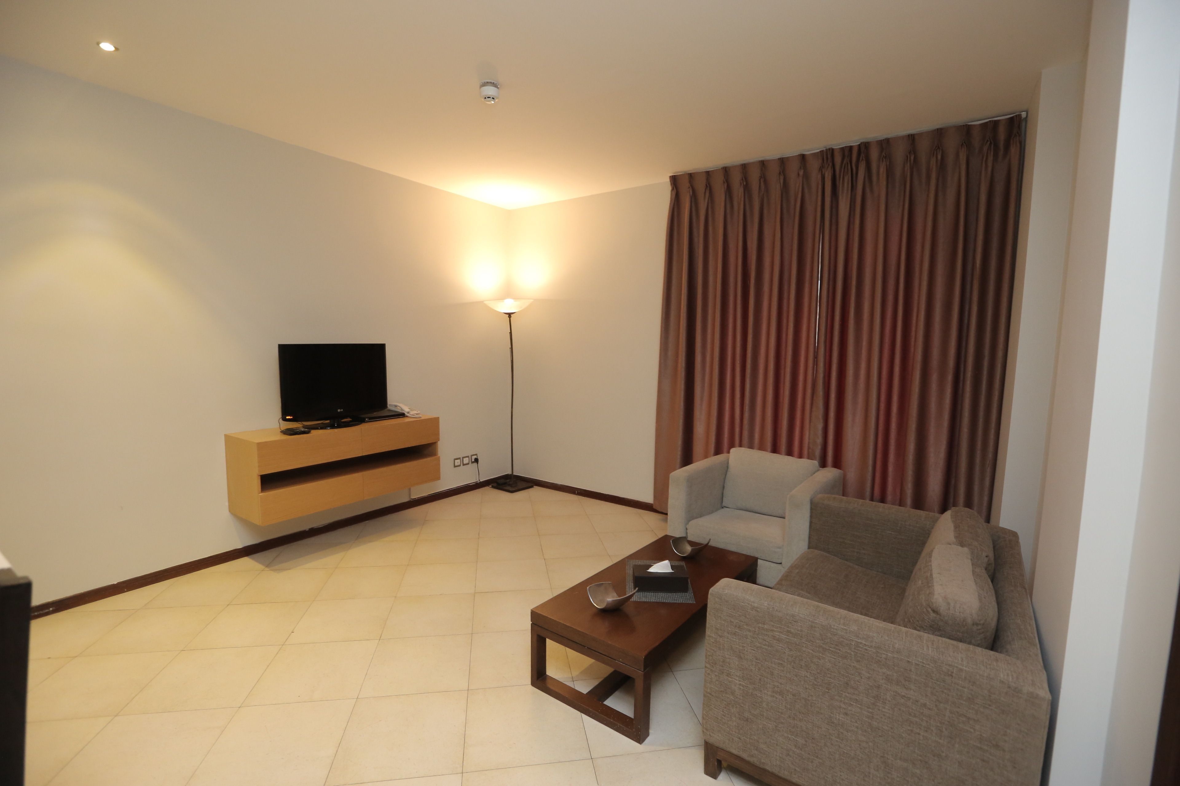 A living room with a sofa, a coffee table, a TV on a wooden stand, and a floor lamp.