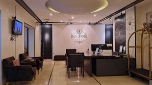 A hotel reception area with a modern design, featuring a reception desk, seating area with chairs, and a television mounted on the wall.