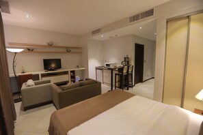 A hotel room with a bed, a sofa, a TV, a desk with a chair, and a kitchenette. - Jabal Amman Hotel (Amman)
