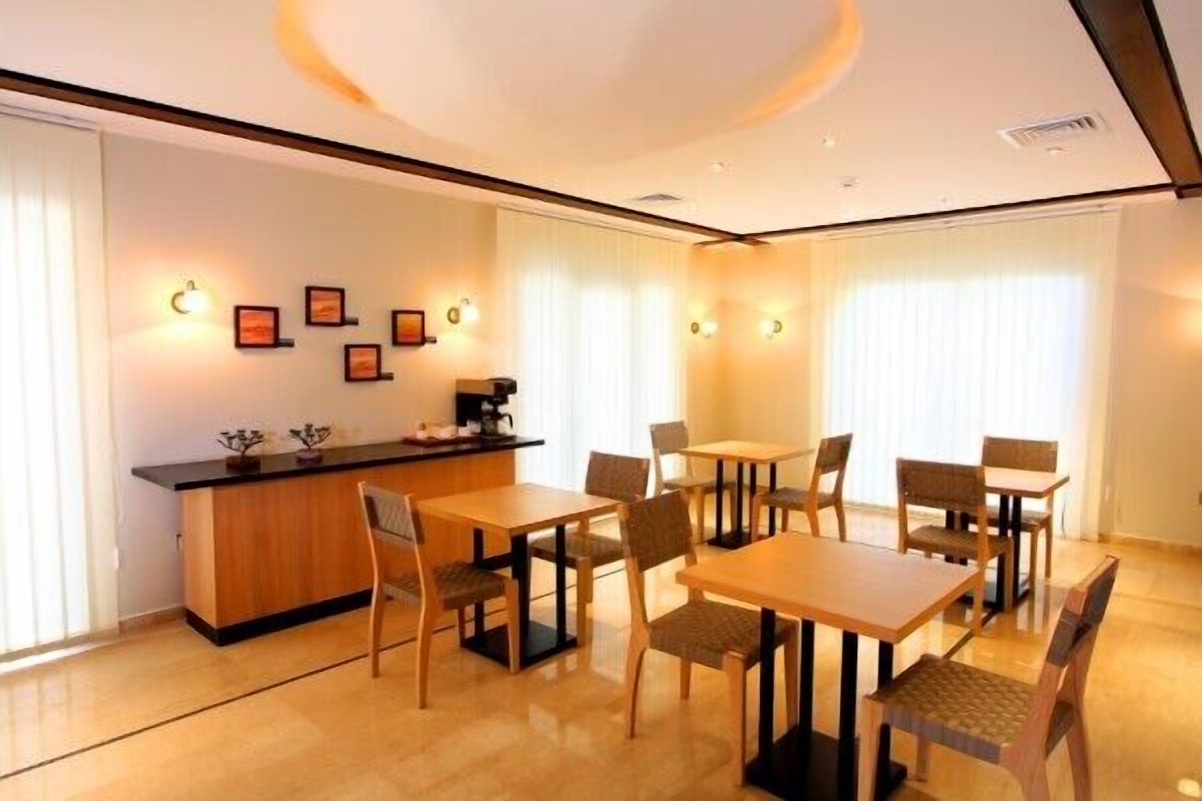 Un comedor moderno con mesas y sillas de madera, una barra y luces fijadas a la pared.