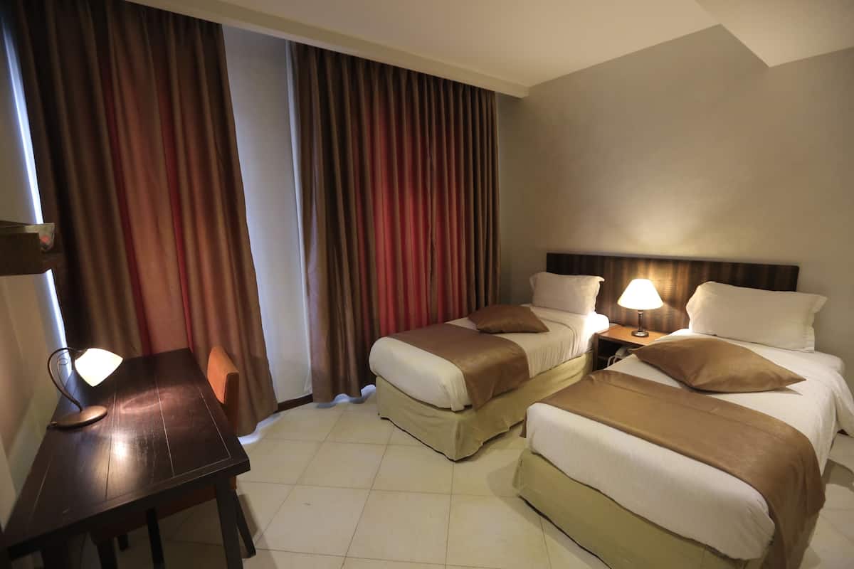 A hotel room with two beds, a desk, and a nightstand with lamps.
