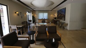 A modern hotel lobby with a central dining area, comfortable seating, and a large painting on the wall.