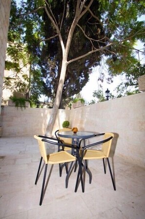 An outdoor patio with a round table and four chairs, surrounded by a low stone wall and a large tree. - Jabal Amman Hotel (Amman)