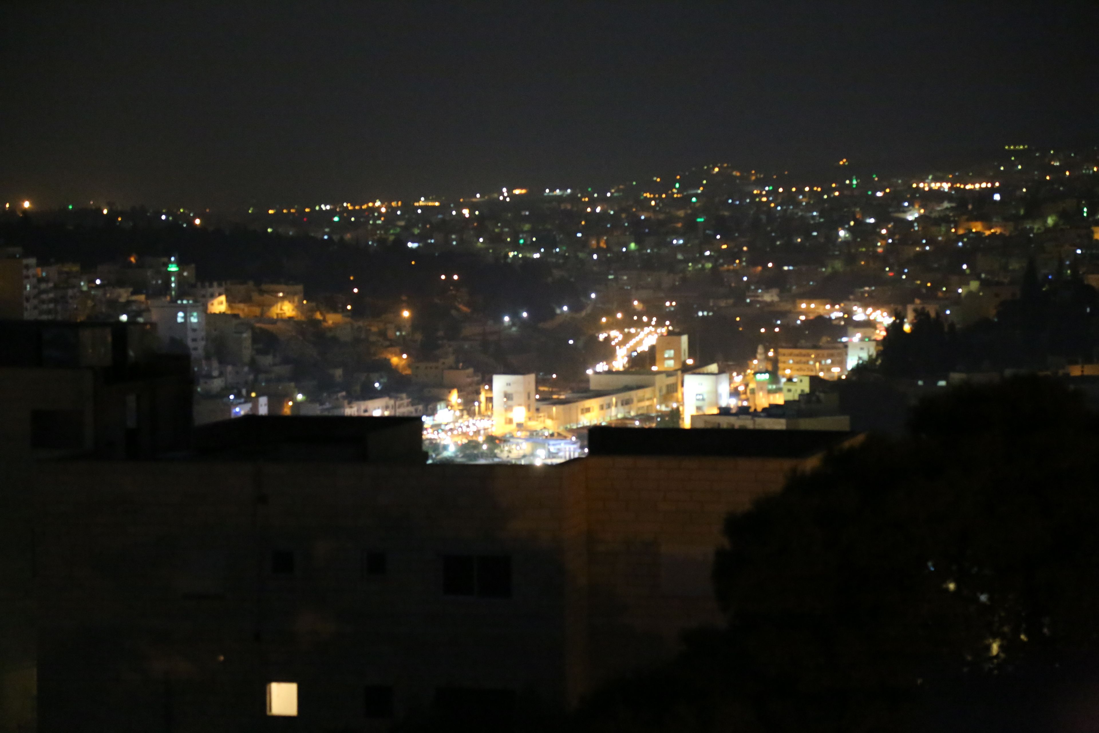 Une vue nocturne d’une ville, avec des bâtiments illuminés et une colline visible au loin.