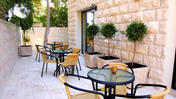 An outdoor patio with round tables and wicker chairs, stone walls, and potted plants.