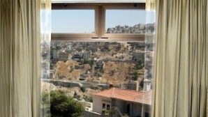 A room with two wooden chairs facing a large window overlooking a cityscape.