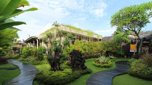 A garden with a winding path, lush greenery, and a building with a green roof. - Gahana Bali Villas (Seminyak)
