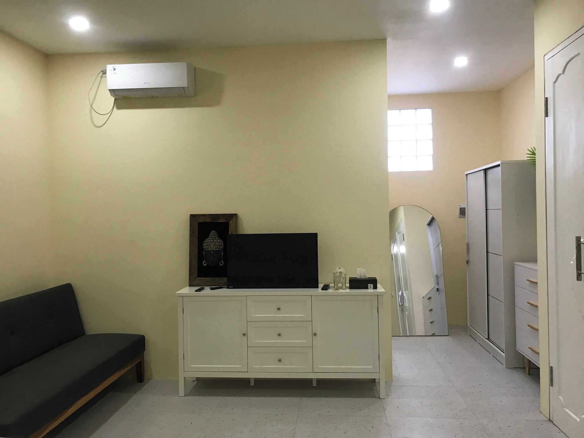 A room with a white cabinet, a black sofa, a framed picture, and a mirror.