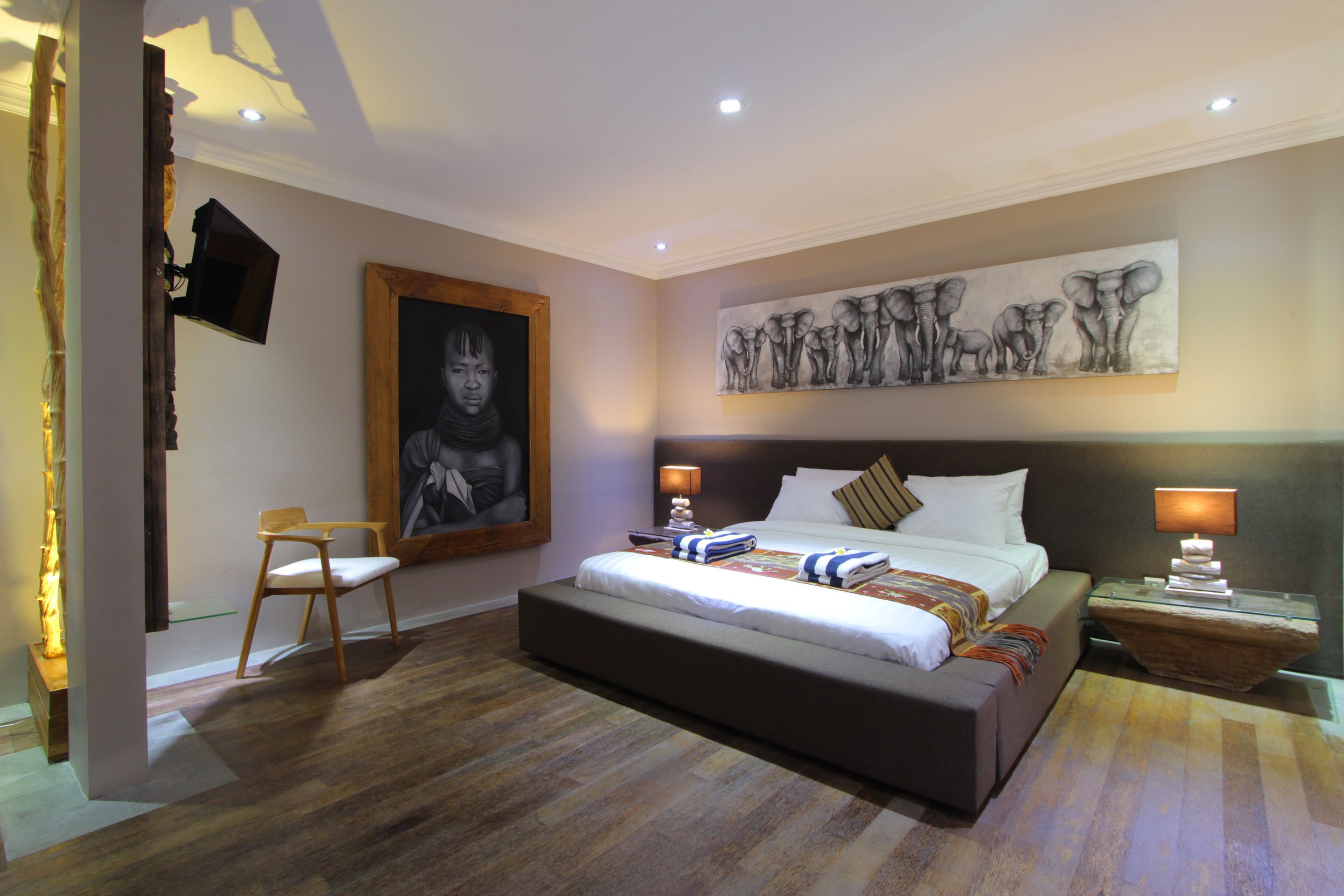 Quarto com uma cama grande, uma cadeira, um quadro e uma televisão fixada na parede.