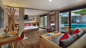 A modern hotel room with a large bed, a desk with a laptop, a sofa, and a view of a swimming pool. - Gahana Bali Villas (Seminyak)