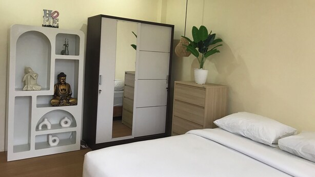 Un dormitorio con cama, armario, espejo, planta en maceta y una pequeña estatua.