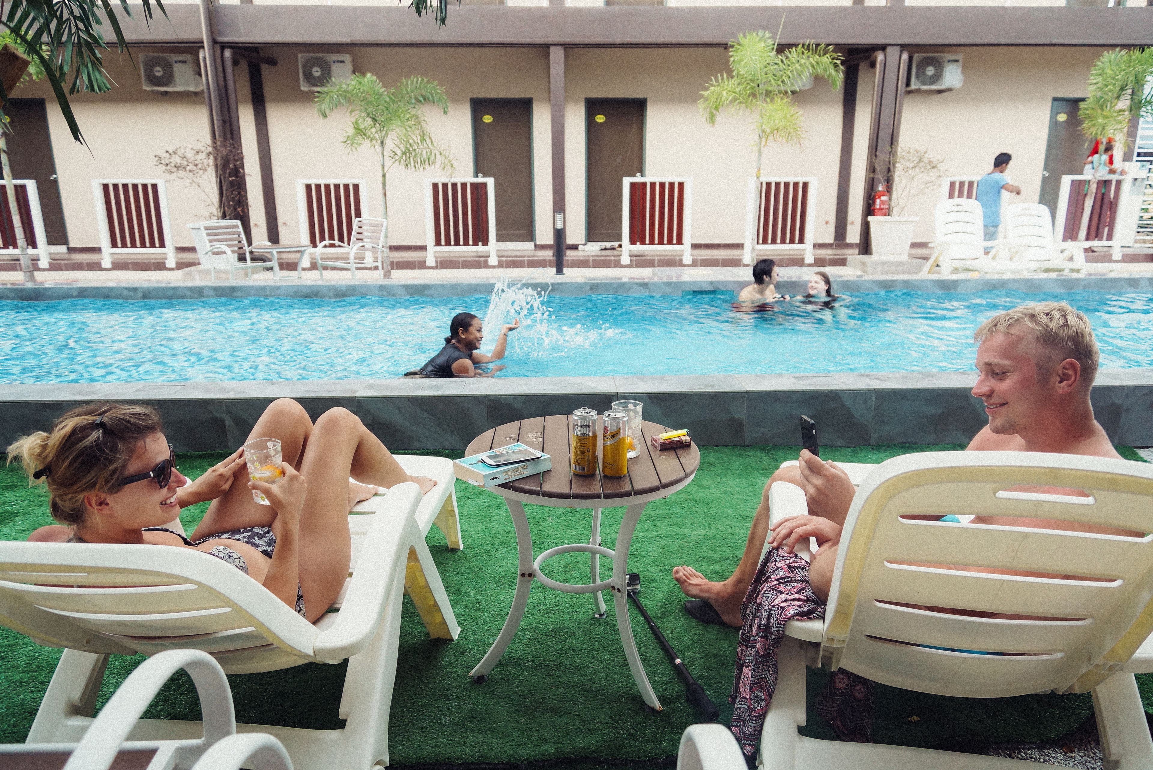 Ein Poolbereich mit Liegestühlen, einem kleinen Tisch mit Getränken und einer Person, die ein Mobiltelefon benutzt.