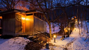 Eine Holzhütte mit beleuchtetem Eingang, umgeben von schneebedecktem Boden und Bäumen.