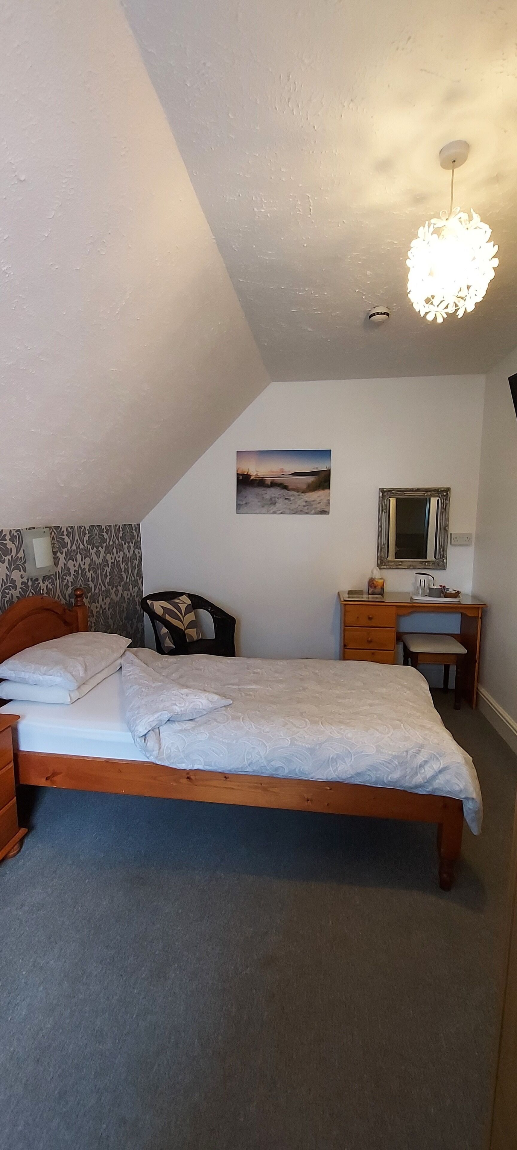 A bedroom with a bed, a desk, a chair, a mirror, and a picture on the wall.