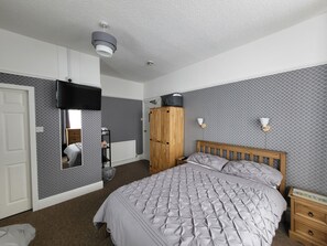A bedroom with a bed, a wardrobe, a TV mounted on the wall, and a small bedside table. - Invernook Hotel (Newquay)