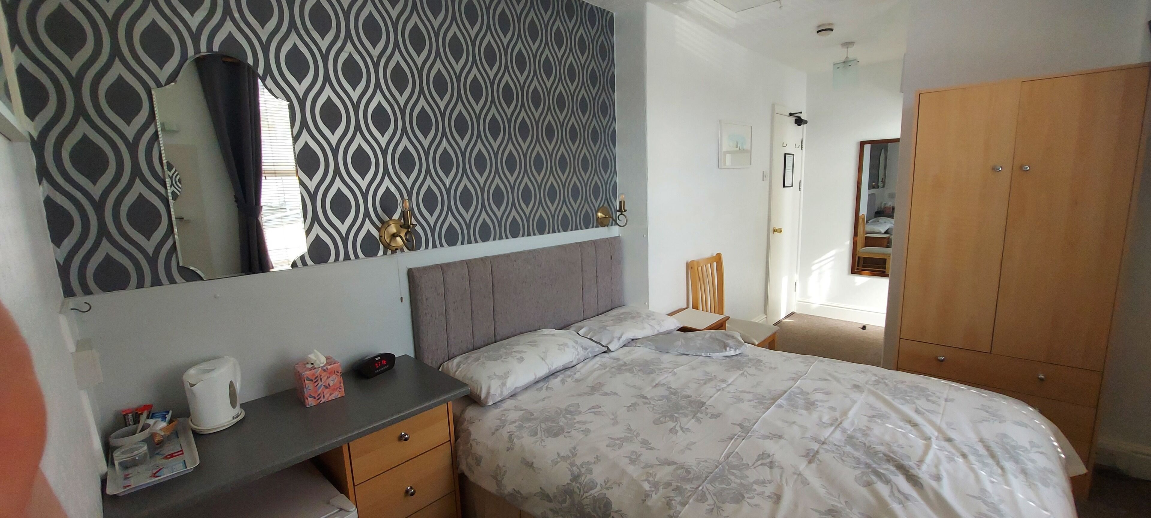 Ein Schlafzimmer mit Bett, Nachttisch, Kommode, Kleiderschrank und einer Wand mit Muster.