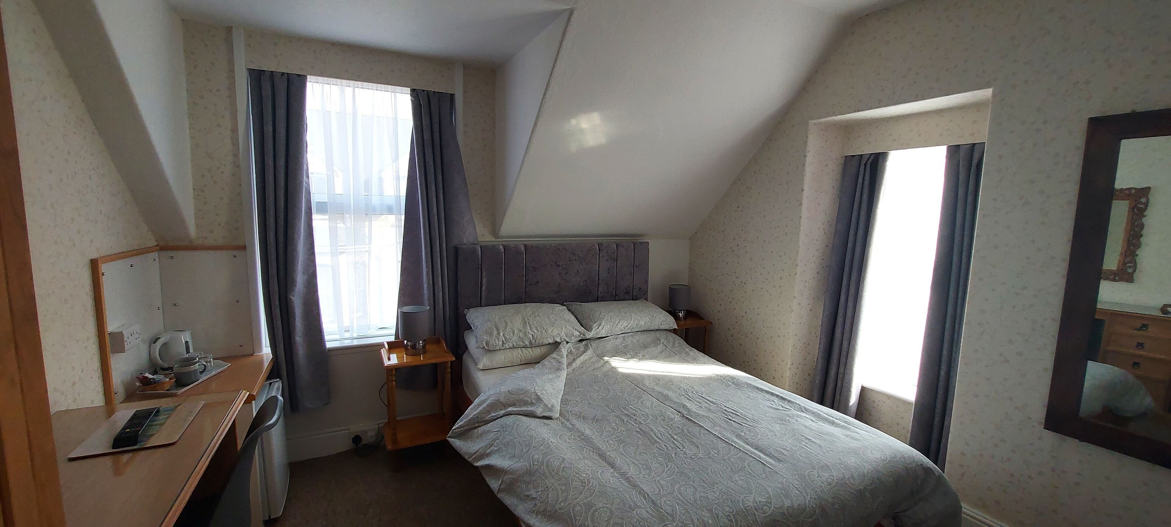 A bedroom with a bed, bedside table, lamp, and a mirror on the wall.