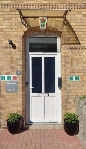 A white door with a glass panel, flanked by two potted plants, a brick wall with decorative tiles, and a sign indicating the building is an inn.