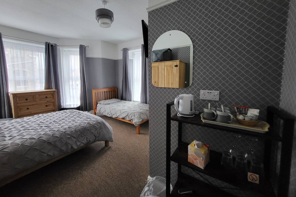 A hotel room with two beds, a wooden dresser, a mirror, and a shelf with toiletries.