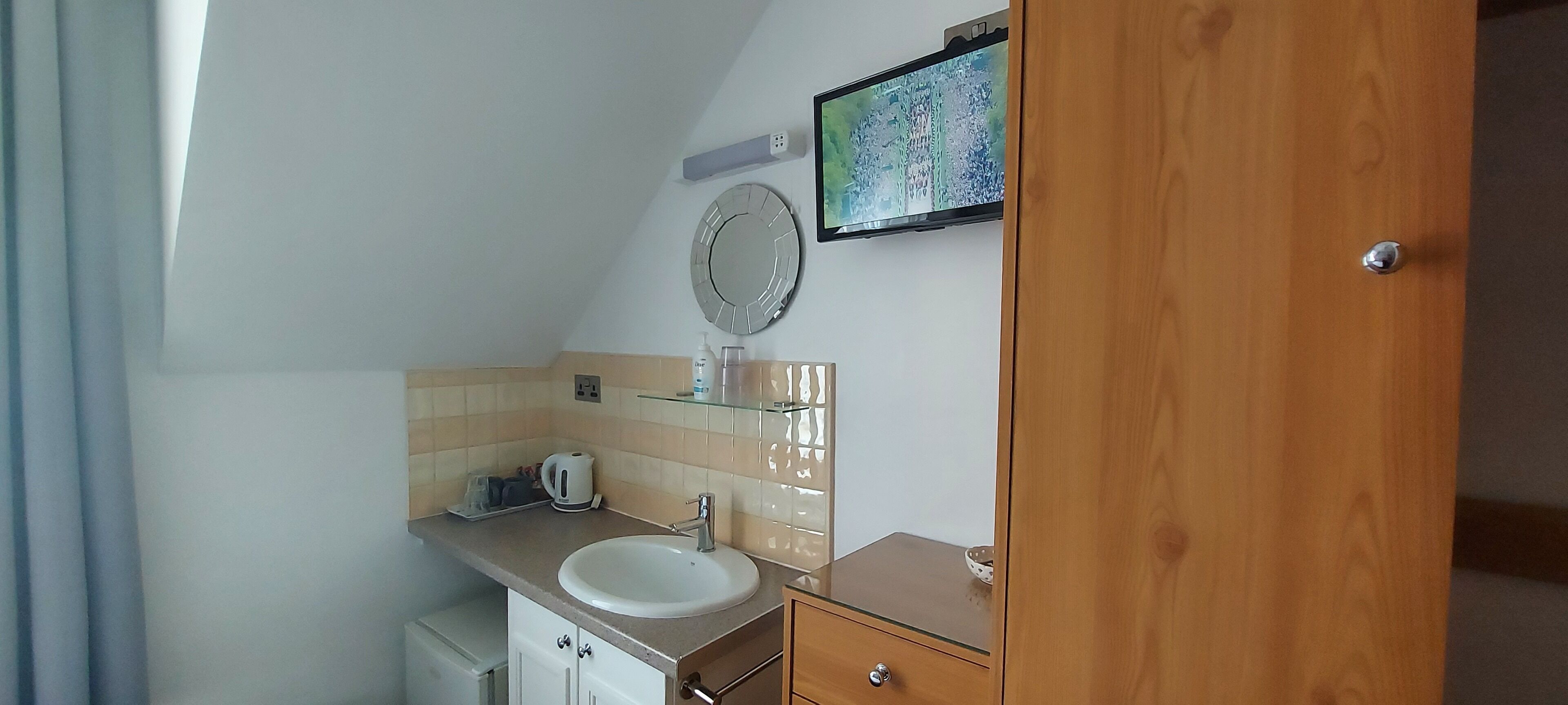 A bathroom with a sink, mirror, and a television mounted on the wall.