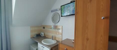 A bathroom with a sink, mirror, and a television mounted on the wall.