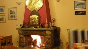 A cozy room with a stone fireplace, a red accent wall, and a chandelier. - Guesthouse Lithos (Kalabaka)