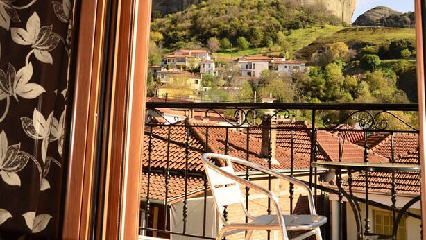 A room with a balcony overlooking a large rock formation and a village below. - Guesthouse Lithos (Kalabaka)