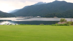 A lake with mountains in the background, a grassy area in the foreground, and a small building near the water's edge. - Hotel & Restaurant Yesterday (Fujikawaguchiko)