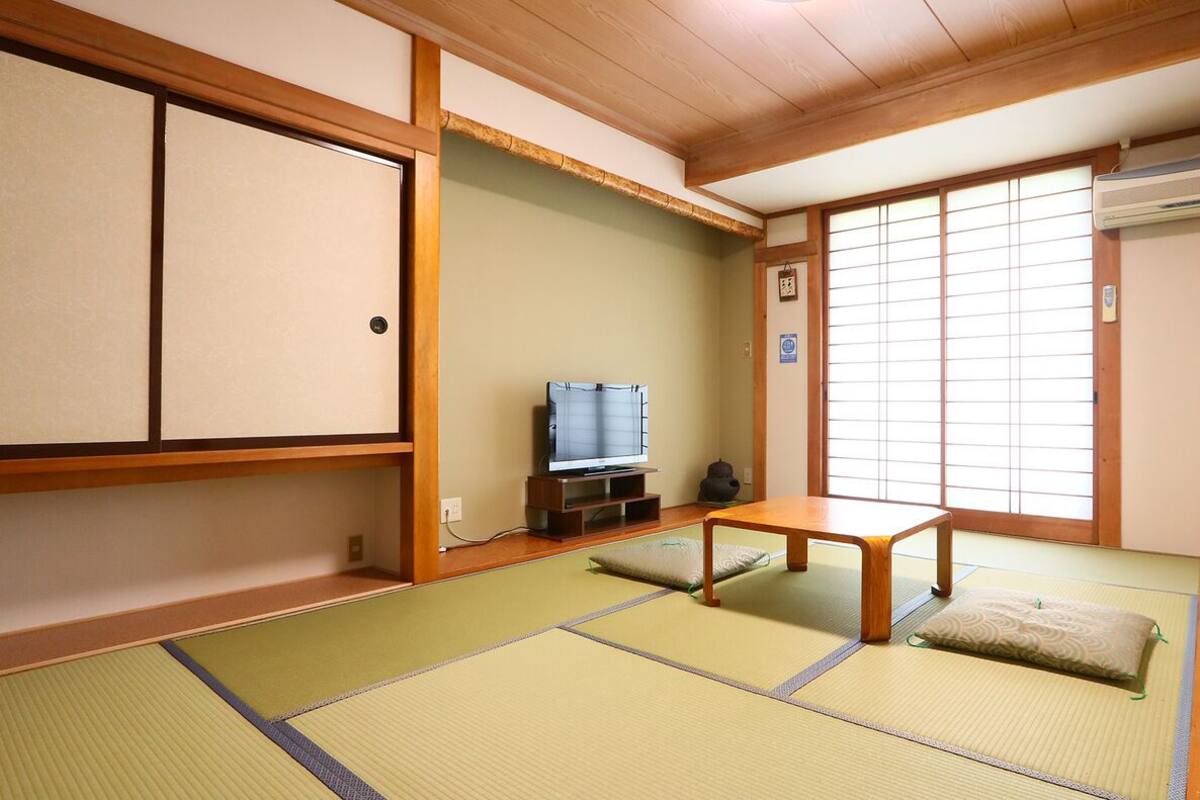A traditional Japanese room with tatami flooring, a television, a table, and sliding doors.