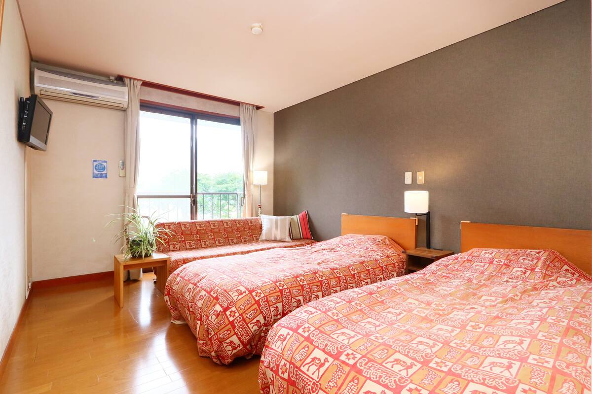 A hotel room with two beds, a small table, a potted plant, and a window with curtains.