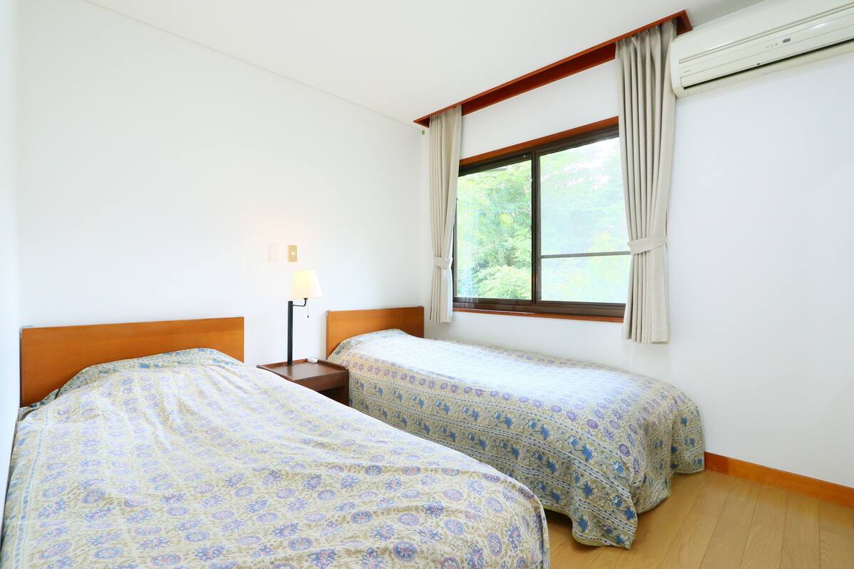 A room with two beds, a nightstand, a lamp, and a window with curtains.