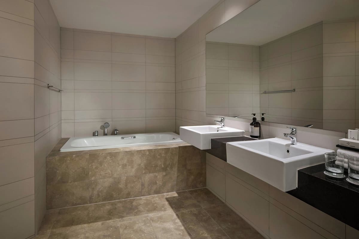 Un baño moderno con una bañera grande, dos lavamanos y un espejo amplio.