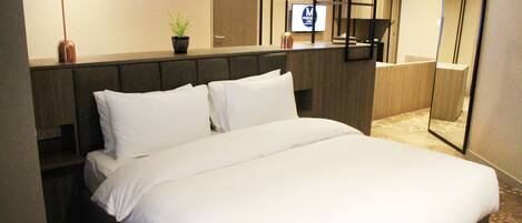 A hotel room with a large bed, a headboard, a bedside table with a lamp, a potted plant, and a mirror.
