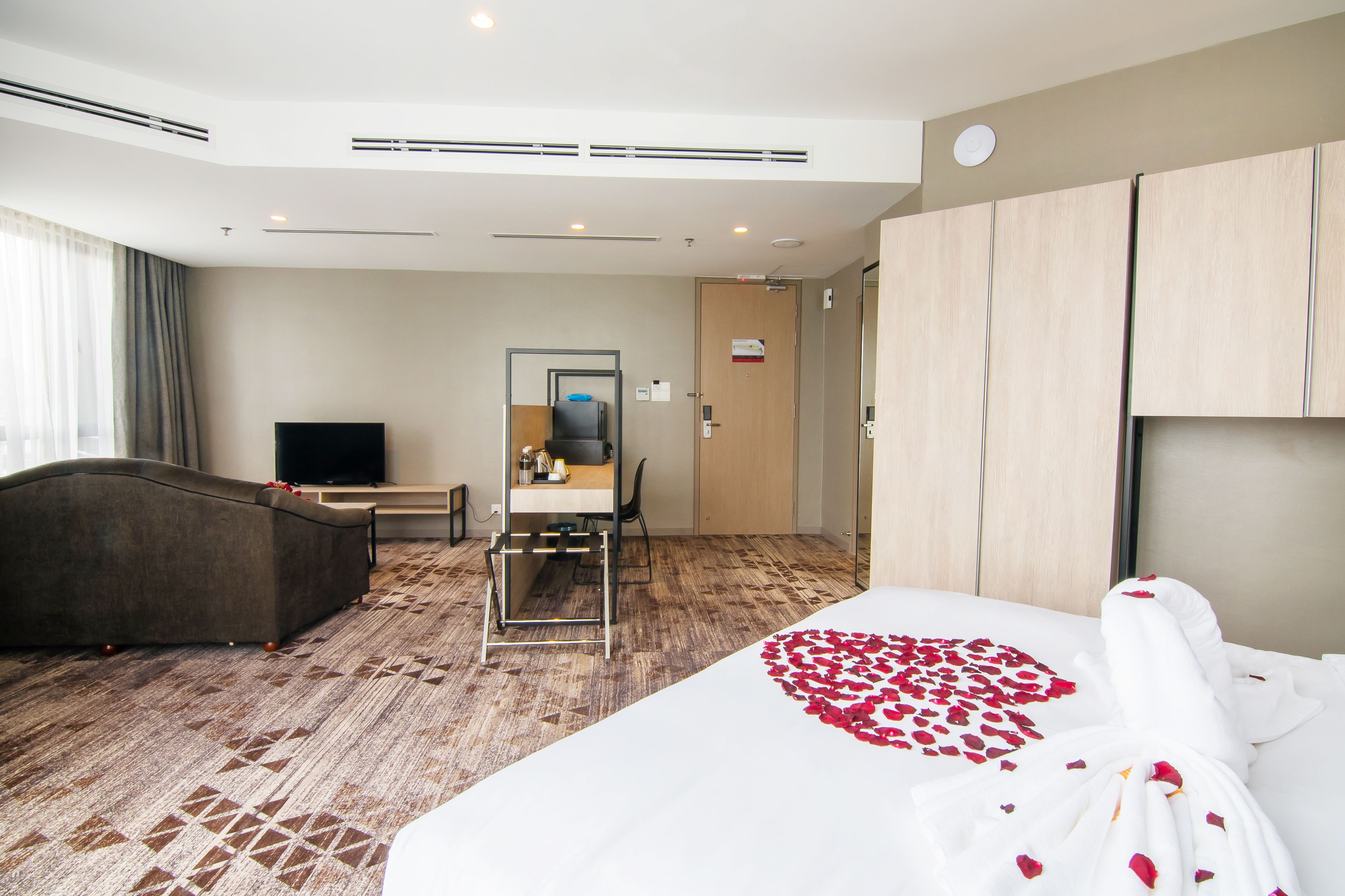 A hotel room with a bed, a desk, a chair, a TV, and a wardrobe.