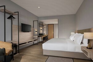 A modern hotel room with a large bed, a desk, a chair, a TV, and a mirror.