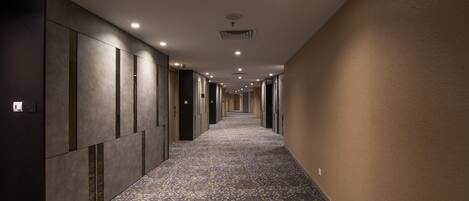 Un pasillo largo y estrecho con alfombra estampada, iluminación empotrada y una serie de puertas a un lado.