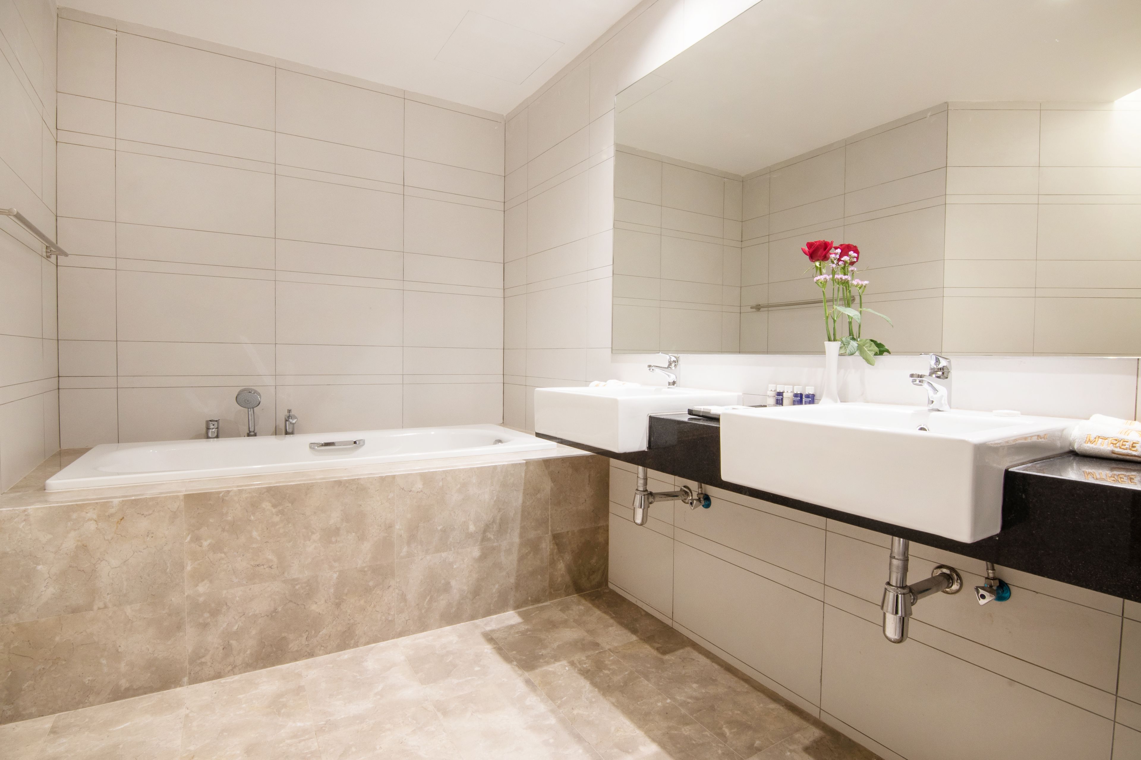 A modern bathroom with a bathtub, two sinks, and a large mirror.
