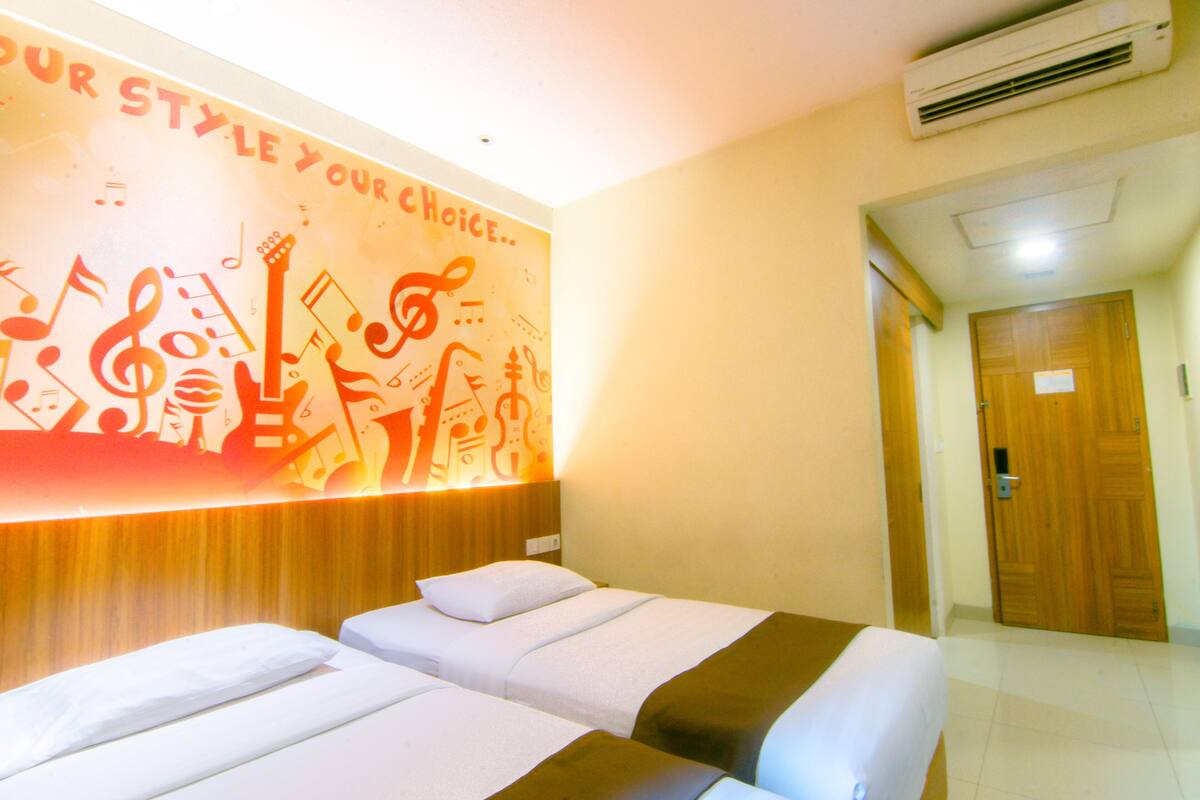 A hotel room with two beds, a wall mural with musical notes, and an air conditioning unit.