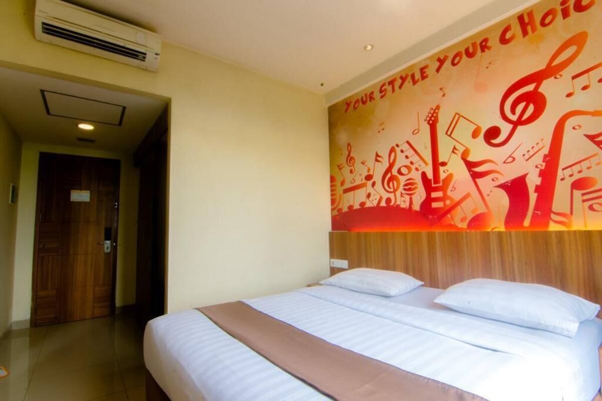 A hotel room with a bed, a wall mural with musical instruments, and an air conditioning unit.