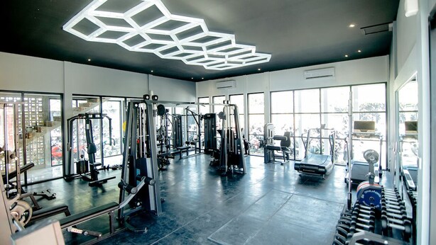 A modern gym with various exercise equipment, large windows, and a geometric light fixture. - Front One Hotel Purwodadi (Purwodadi)