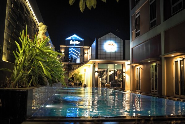 An outdoor swimming pool with a view of a building with illuminated signage in the background. - Front One Hotel Purwodadi (Purwodadi)