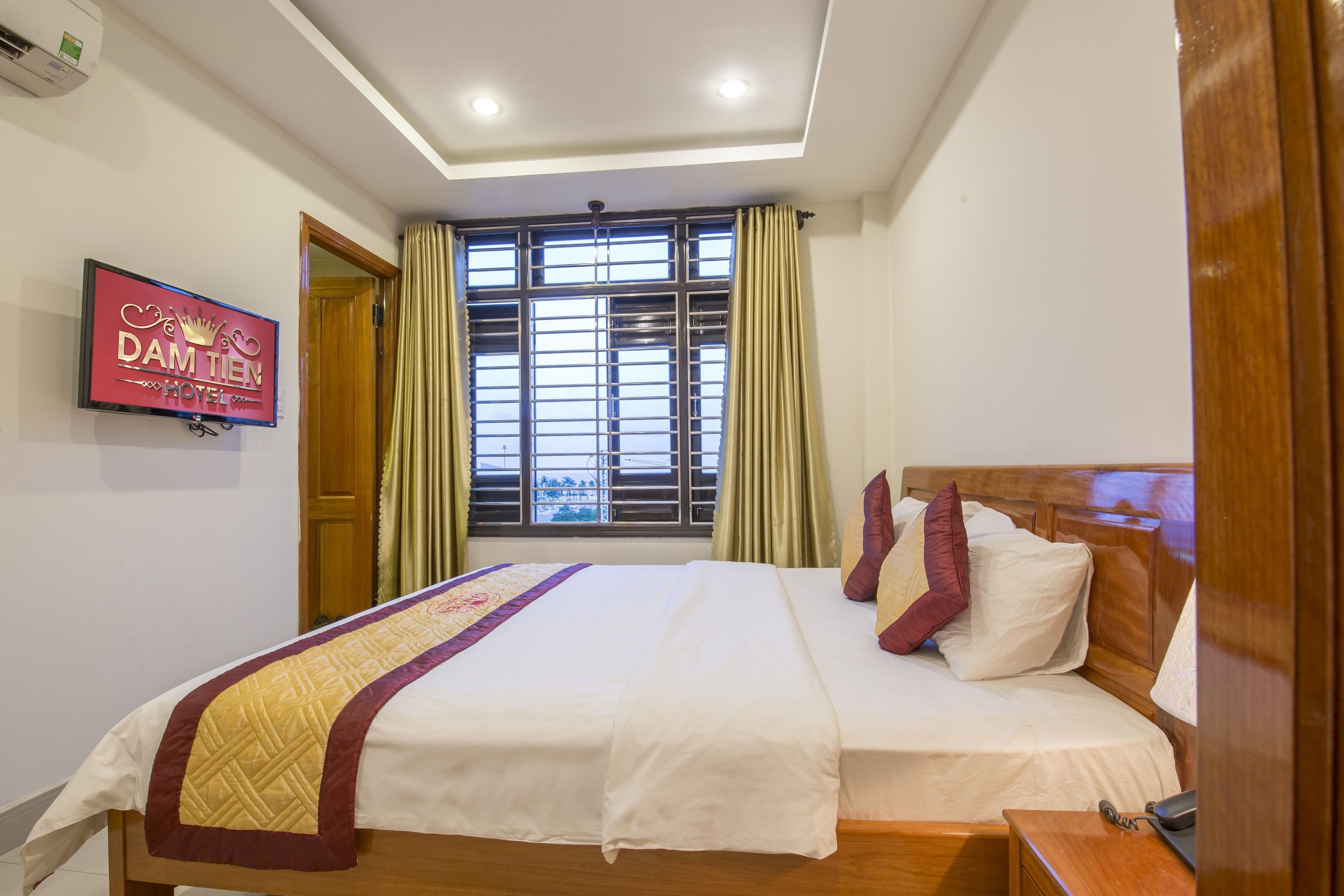 A hotel room with a large bed, a TV on the wall, and a window with curtains.