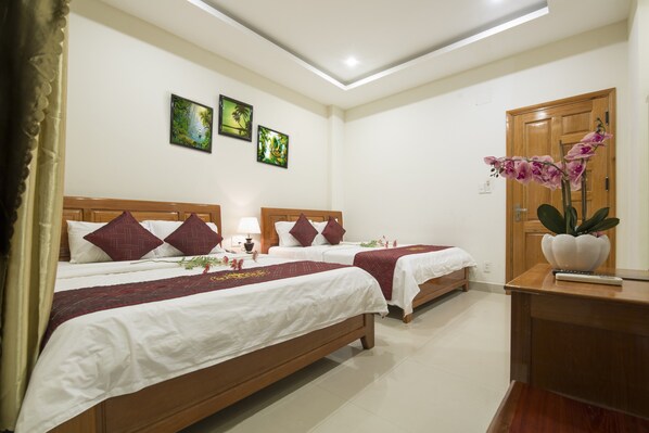 A hotel room with two beds, a wooden headboard, a desk, and a potted orchid.