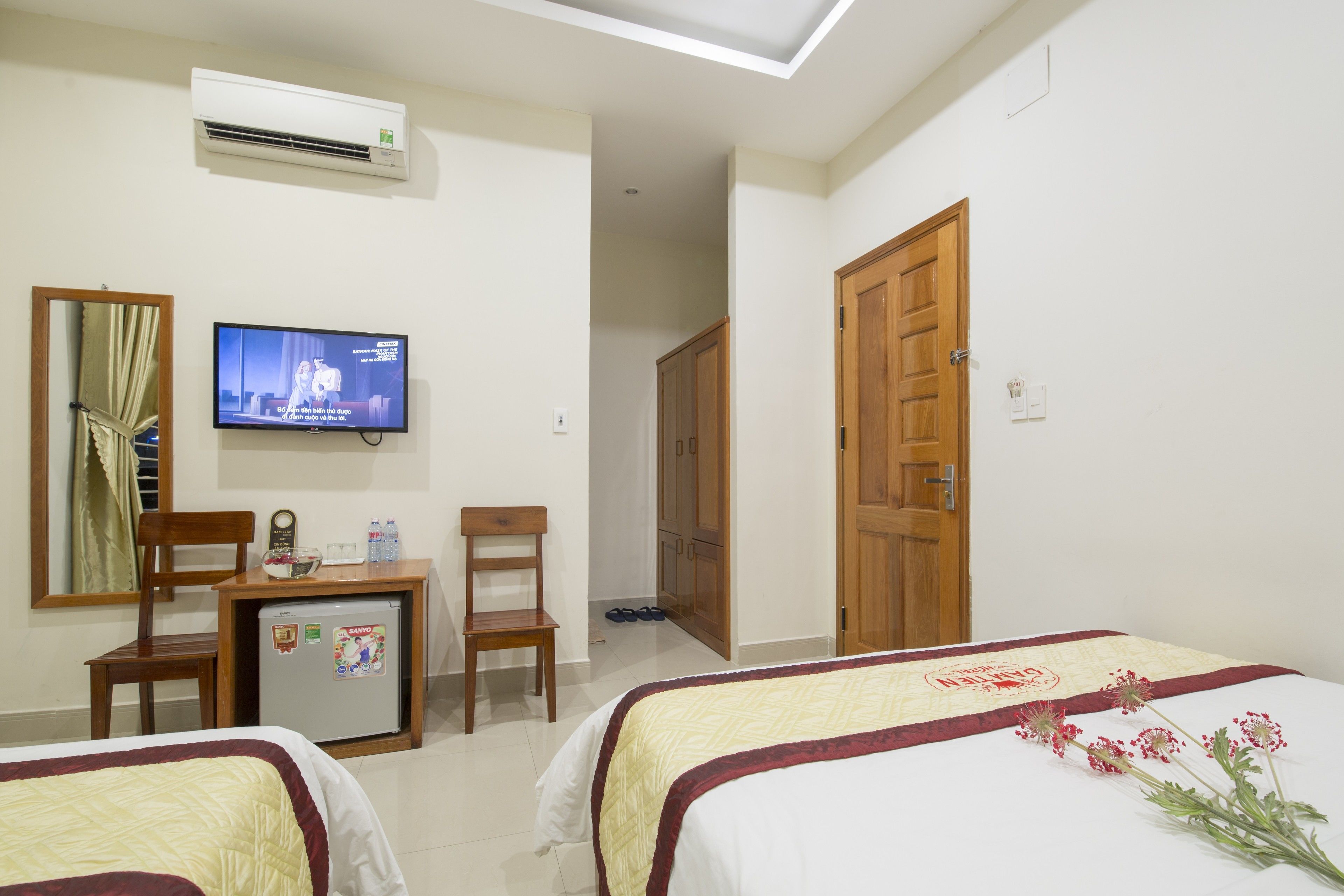 A hotel room with two beds, a TV, a desk with a refrigerator, a chair, and a wardrobe.