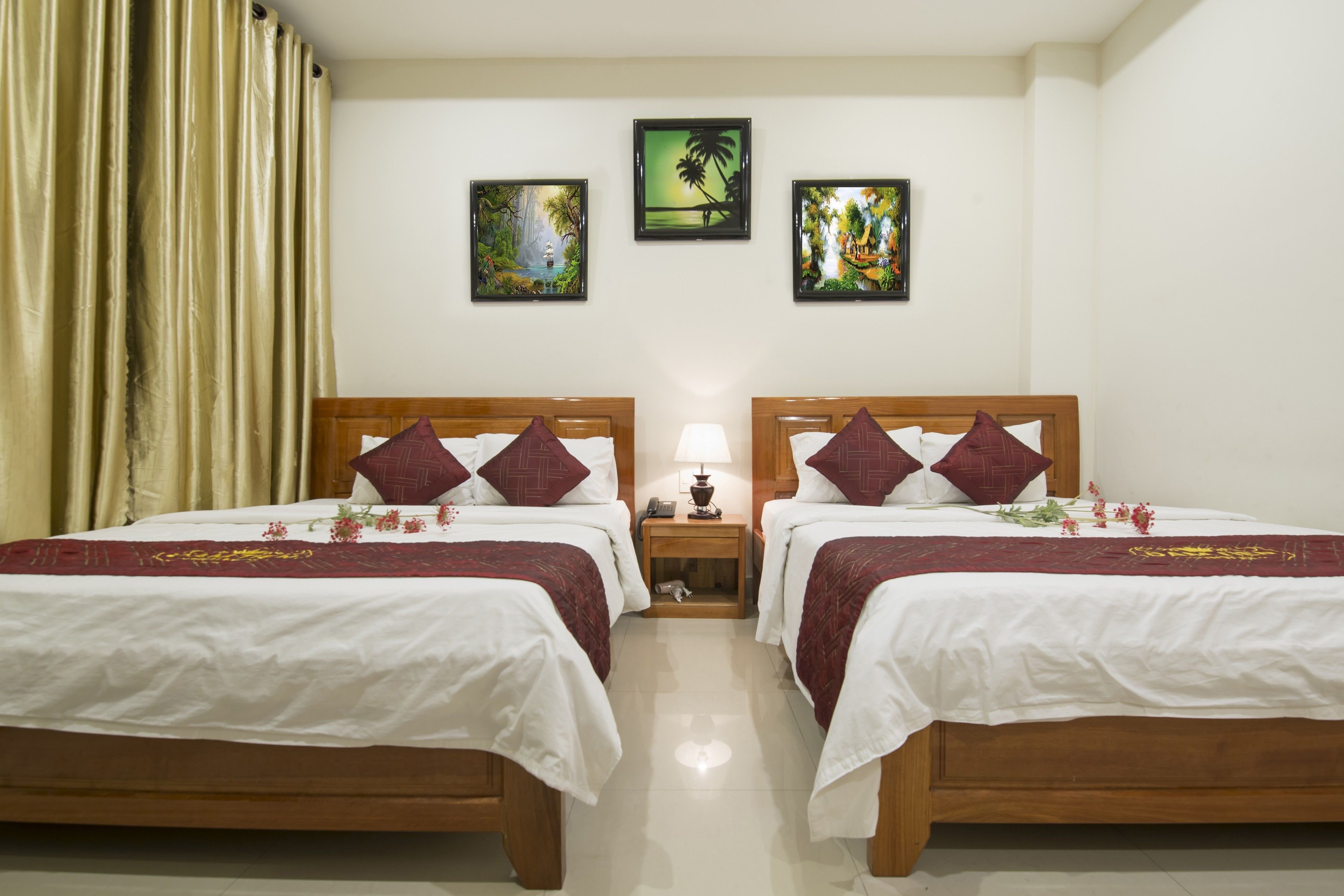 A hotel room with two beds, a nightstand with a lamp, and three framed pictures on the wall.